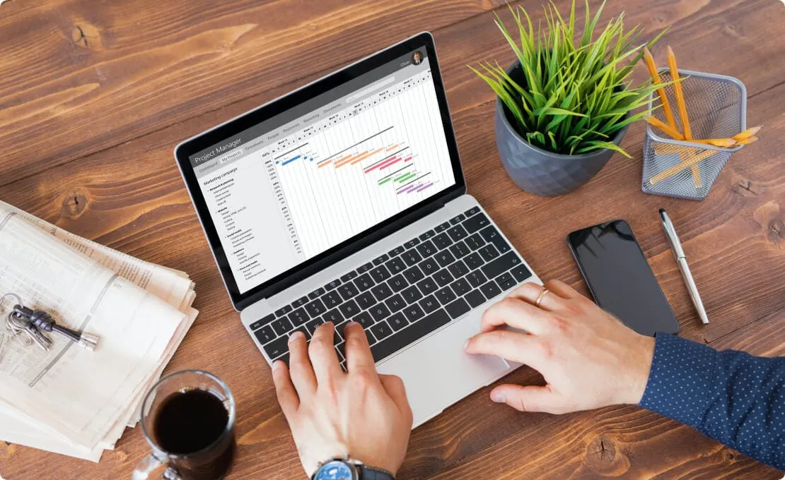 Overhead view of hands on a laptop showing a project schedule with a Gantt chart